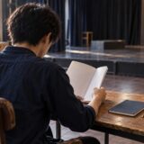 稽古場で台本を読み、進路を考える青年のイメージ